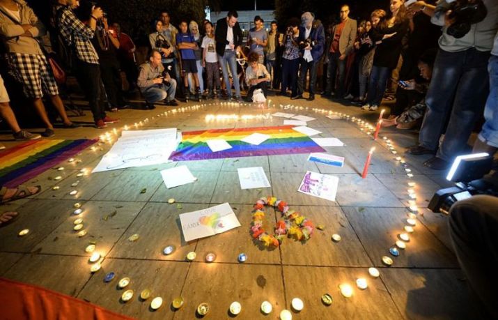 People gathered around a Pride flag and memorial candles lit honoring LGBTQ+ people