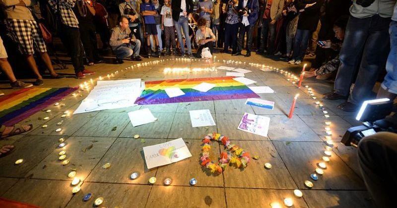 People gathered around a Pride flag and memorial candles lit honoring LGBTQ+ people